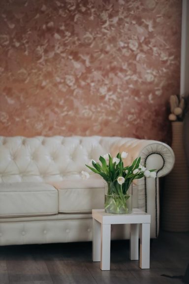 Beige Couch vor einer rosefarbenen Wand, daneben ein Tisch mit einem Blumengesteck.