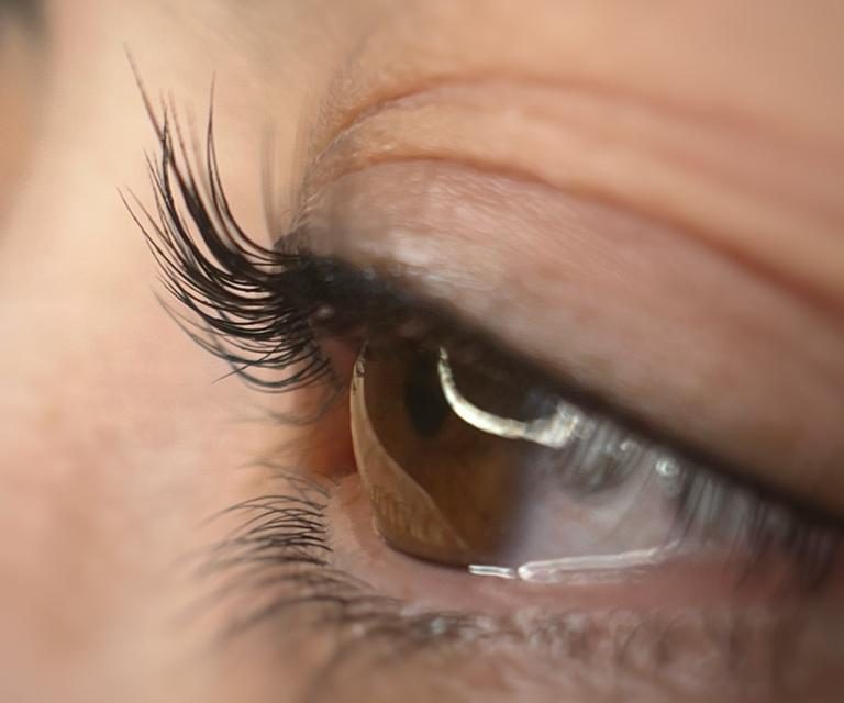 Nahaufnahme eines menschlichen Auges mit langen Wimpern und brauner Iris.